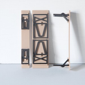 May include: A disassembled wooden table with black accents. The table components are beige with black geometric designs and supports. The pieces are arranged against a white background, showcasing the table's construction.
