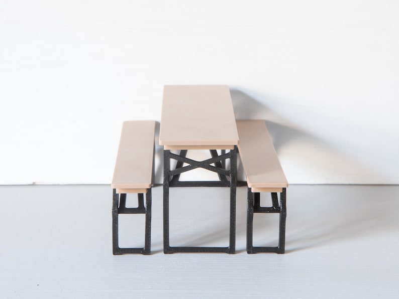 May include: A miniature picnic table set with a light wood tabletop and benches. The table and benches have black metal frames. The set is designed for a dollhouse or miniature scene.