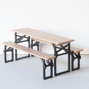 May include: A miniature picnic table with attached benches. The tabletop and benches are light brown, supported by black, angled legs. The table measures approximately 12 inches long, 6 inches wide, and 5 inches high.