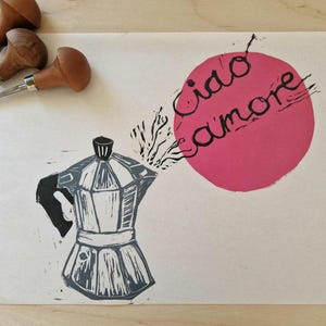 Könnte beinhalten: Ein Druck einer Kaffeemaschine mit den Worten "Ciao Amore" in schwarzer Schrift auf einem rosa Kreis. Die Kaffeemaschine ist grau und schwarz. Drei Werkzeuge mit Holzgriffen befinden sich in der oberen linken Ecke.
