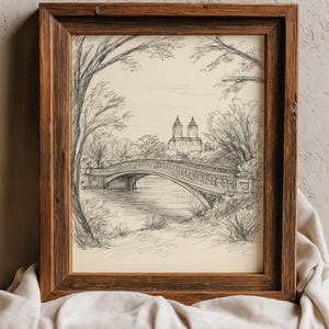 以下が含まれることがあります： 水上の橋の鉛筆スケッチが額装されています。背景には木々と建物があります。アートワークは素朴な茶色の木製フレームに入っており、白い布の上に置かれています。スケッチは白黒です。