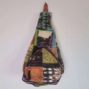Può includere: Borsa a tracolla patchwork con una varietà di colori e motivi. La borsa presenta uno scomparto principale con cerniera, più tasche e un nappa decorativa. Il design include un simbolo Om e una spirale.