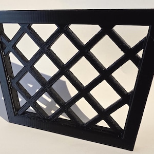 May include: A black, geometric trellis panel with a diamond pattern. The panel is made of a solid material and is angled slightly, casting a shadow on the white surface behind it. The design is a decorative element.