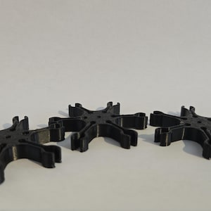 Puede incluir: Tres objetos negros en forma de estrella están dispuestos sobre una superficie blanca. Cada objeto tiene múltiples brazos curvos que se extienden desde un centro central. Los objetos parecen estar hechos de plástico o un material similar.