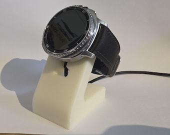 May include: A silver smartwatch with a black leather strap sits on a white charging stand. The watch has a black screen and a rotating bezel. A black charging cable is connected.
