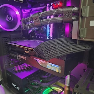 May include: A computer tower with internal components illuminated by purple and green LED lights. The components include a graphics card with the text "AORUS GeForce RTX", a power supply, and cooling fans. Braided cables are visible.