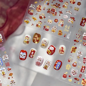 May include: Nail art stickers with Lunar New Year themes. The stickers feature cartoon animals, flowers, and Chinese characters in red, gold, and white. Some stickers are applied to painted nails, showcasing the designs.