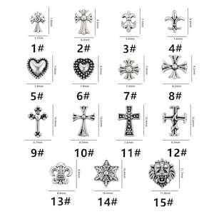 May include: A collection of silver-colored metal charms in various designs, including crosses, hearts, fleur-de-lis, and a lion's head. Each charm has a number and measurements in millimeters. The charms are suitable for jewelry making or crafting.