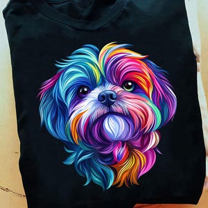 Puede incluir: Camiseta negra con una ilustración colorida y estilizada de la cara de un perro. El pelaje del perro está representado en tonos vibrantes de azul, morado, amarillo y naranja. El perro tiene ojos grandes y expresivos y una pequeña nariz negra.