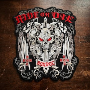 May include: A black embroidered patch featuring a central skull with red eyes, wings, and a sword. The text RIDE OR DIE is arched at the top in red, with the word BONDOC on a banner below the skull and the letters B O N D O C on two red crosses.