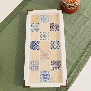 Peut inclure: Un plateau de service rectangulaire avec un cadre blanc et des carreaux décoratifs incrustés. Le plateau présente un motif de carrés beiges entrecoupés de carreaux bleus et blancs. Les coins sont renforcés de métal couleur laiton.