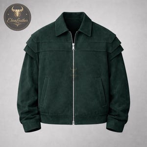 Könnte beinhalten: Dunkelgrüne Cordjacke mit silbernem Reißverschluss. Die Jacke hat einen Kragen, zwei Vordertaschen und geschichtete Schulterdetails. Das EbonLeather-Logo befindet sich in der oberen linken Ecke.