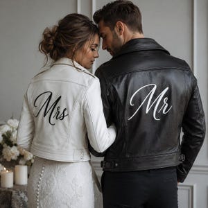 May include: A pair of leather jackets, one white and one black, worn by a couple. The white jacket has "Mrs" written on the back in cursive, while the black jacket has "Mr". Both jackets are in a classic biker style.