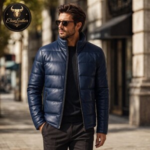 K&ouml;nnte beinhalten: Marineblaue Leder-Steppjacke mit hohem Kragen und Rei&szlig;verschluss. Die Jacke hat horizontale Steppn&auml;hte und wird mit einer schwarzen Hose getragen. Das EbonLeather-Logo ist sichtbar.