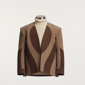 Könnte beinhalten: Eine braune und beige Jacke mit einem einzigartigen Design, getragen über einem cremefarbenen Rollkragenpullover. Die Jacke hat ein markantes Muster mit geschwungenen, dunkelbraunen Abschnitten. Die Ärmel sind lang, und die Jacke scheint aus einem strukturierten Stoff zu sein.
