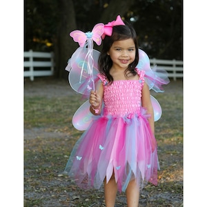 May include: A pink fairy costume featuring a smocked bodice, a multi-layered tulle skirt in shades of pink and blue, and attached iridescent wings. The outfit includes a matching pink butterfly hair bow and a wand topped with a pink butterfly.