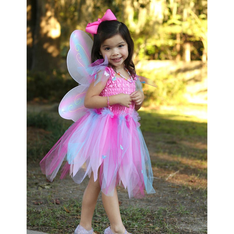 May include: A pink fairy costume featuring a sleeveless bodice with a smocked texture, a multi-layered tulle skirt in shades of pink and light blue, iridescent butterfly wings, and a large pink hair bow with a matching beaded necklace.