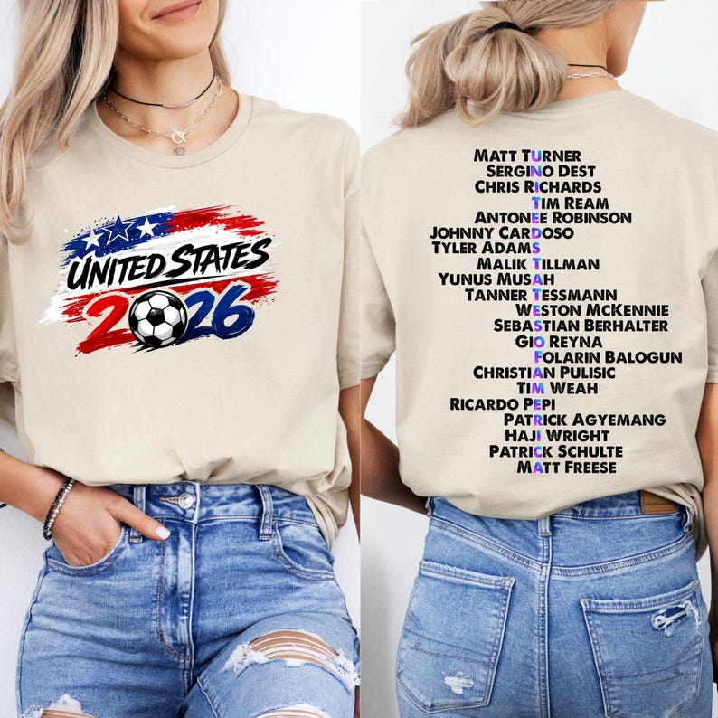 May include: Beige t-shirt with the text "UNITED STATES 2026" and a soccer ball graphic. The back of the shirt lists soccer player names. The shirt is made of a soft material.