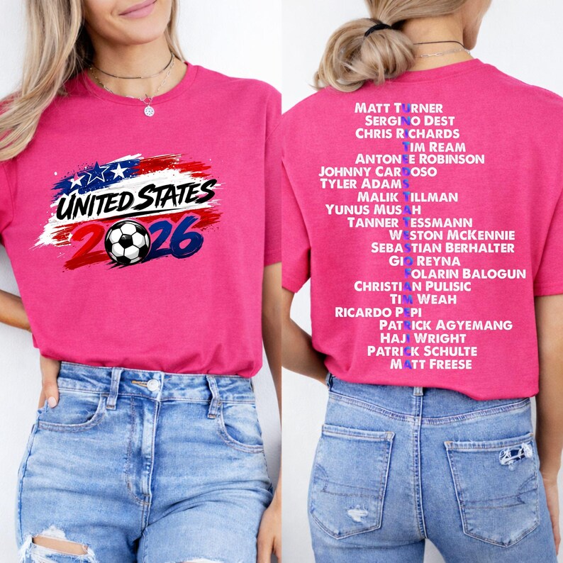 May include: A magenta t-shirt with the text "UNITED STATES 2026" and a soccer ball design. The back of the shirt lists names. The shirt is worn with blue jeans. The shirt is a casual wear item.