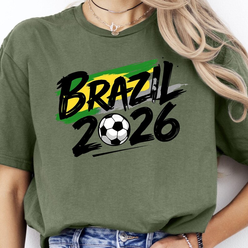 Op de afbeelding: Olijfgroen t-shirt met het woord "BRAZIL" in zwart, met een geel en groen streepontwerp, en het jaar "2026" in zwart met een voetbalafbeelding. Het shirt heeft een casual stijl.