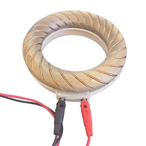 Könnte beinhalten: Ein kreisförmiges elektrisches Bauteil mit einem hellbraunen, gerippten Außenring und kupferfarbener Verkabelung. Das Bauteil hat einen weißen Innenraum und zwei Anschlüsse mit roten und schwarzen Drähten.