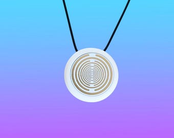 May include: A circular pendant featuring a white outer rim and a gold-colored center with a series of concentric circles radiating from the middle. The pendant is suspended from a thin black cord, creating a simple and geometric design element.