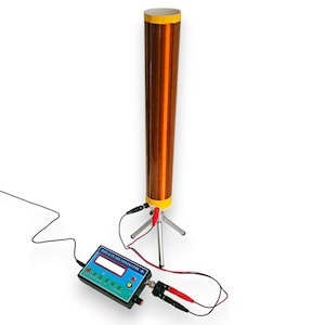 Op de afbeelding: Een Rife & Clark Generator, een wetenschappelijk apparaat, heeft een lange, koperkleurige spoel met gele en witte accenten. Het staat op een klein statief en is verbonden met een bedieningskast met een digitaal display en diverse knoppen. Zwarte en rode draden lopen van het apparaat.