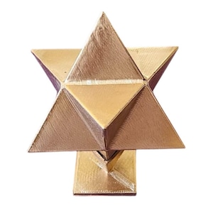 Könnte beinhalten: Ein goldfarbenes, dreidimensionales sternförmiges Objekt mit einem geometrischen Design aus mehreren dreieckigen Flächen. Die Struktur ist auf einem kleinen, quadratischen Sockel montiert und weist eine texturierte Oberfläche auf.