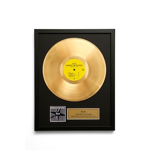 May include: Framed gold record of R.E.M.'s "Automatic for the People" album. The record is centered on a black frame, with a yellow label. A plaque below the record displays the album title and release date.