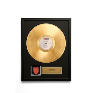 Peut inclure: Disque d'or encadré de l'album de Phil Collins "No Jacket Required". Le disque est présenté dans un cadre noir, avec une petite photo de Phil Collins et une plaque avec les détails de l'album. Le disque a une finition dorée.