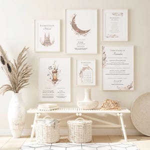 May include: A collection of framed art prints with floral and calligraphy designs, including a crescent moon, a lantern, and a calendar. The prints are in neutral tones and feature the word "Ramadan". The art is displayed above a white bench with woven baskets.