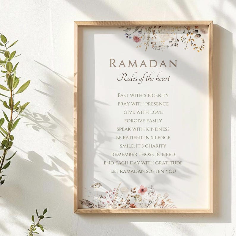 May include: A framed print with the text "RAMADAN Rules of the heart" in a light brown font. The print includes a list of rules and is decorated with floral accents in shades of pink, purple, and brown. The frame is made of light-colored wood.
