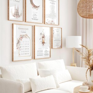 May include: A collection of framed wall art with a Ramadan theme. The art features floral and architectural designs, along with the words "Ramadan Mubarak" and "Ramadan Calendar". The frames are a light brown color, and the overall aesthetic is soft and inviting.