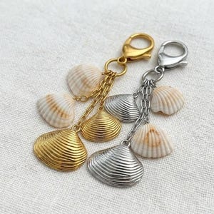 Op de afbeelding: Twee sleutelhangers met schelpenbedels. Eén sleutelhanger heeft een goudkleurige sluiting, ketting en bedels. De andere heeft een zilverkleurige sluiting, ketting en bedels. Beide sleutelhangers hebben echte schelpen.