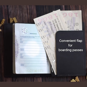 K&ouml;nnte beinhalten: Schwarzer Leder-Reisepasshalter mit praktischer Klappe f&uuml;r Bordkarten. Der Reisepasshalter ist ge&ouml;ffnet und zeigt einen Reisepass und Tickets. Der Text "Convenient flap for boarding passes" ist auf der Klappe zu sehen.
