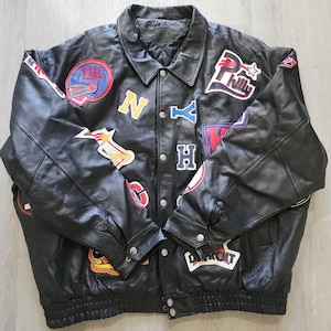 May include: Black leather jacket with multiple colorful patches featuring team logos and city names. The jacket has a button-up front, a collar, and a ribbed hem. The patches include "NY", "Philly", and "Detroit".
