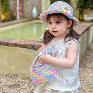 May include: A colorful, crocheted hat with a white flower accent and matching purse. The hat and purse feature a rainbow of pastel colors, including pink, yellow, blue, and green. The purse has a wooden button closure.
