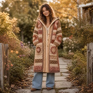 May include: A long, hooded crochet coat in shades of brown, beige, and rose. The coat features a geometric pattern with square pockets and a button-up front. The person is wearing blue jeans and brown shoes.