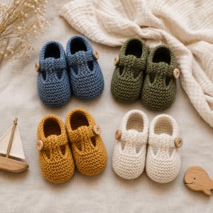 Può includere: Quattro paia di scarpine per bambini lavorate a maglia in blu, verde, giallo e bianco. Ogni paio presenta uno stile Mary Jane con chiusura a bottone. Le scarpe sono disposte su un tessuto colorato neutro, con elementi decorativi in legno.