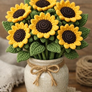 May include: A handcrafted bouquet of crocheted sunflowers in a ceramic vase. The sunflowers have yellow petals and brown centers, with green leaves. The vase is tied with twine, creating a rustic, charming floral arrangement.