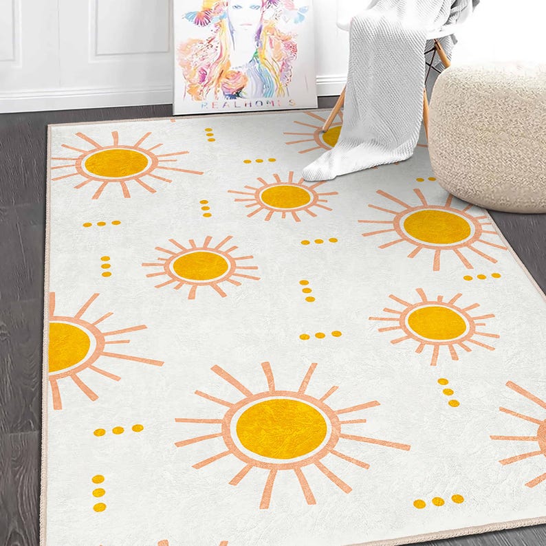 May include: A white area rug with a repeating pattern of yellow suns and peach-colored rays. The rug is rectangular and has a cream-colored border. The design is modern and cheerful, suitable for a living room or bedroom.