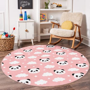 Op de afbeelding: Een ronde roze vloerkleed met een herhalend patroon van panda gezichten, witte wolken en kleine sterren. Het vloerkleed is gemaakt van zacht materiaal en is geschikt voor een kinderkamer of kinderkamer. De diameter van het vloerkleed is ongeveer 152 cm.