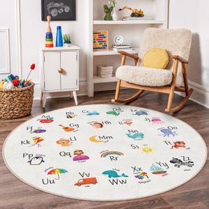 Könnte beinhalten: Ein runder, cremefarbener Kinderteppich mit dem Alphabet und bunten Illustrationen. Jeder Buchstabe hat ein passendes Bild, wie ein Apfel für 'A' und ein Zebra für 'Z'. Geeignet für ein Spielzimmer oder Kinderzimmer.