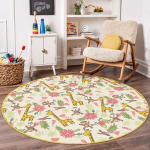 Può includere: Un tappeto rotondo a tema giungla. Presenta giraffe gialle, scimmie marroni, fiori rosa e foglie verdi su uno sfondo color crema. Il tappeto ha un bordo giallo ed è posizionato su un pavimento in legno.