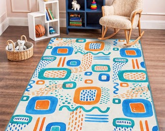 May include: A rectangular area rug with a colorful, abstract design. The rug features a cream-colored background with blue, orange, and teal geometric shapes and patterns. The rug has a blue border and is placed on a wooden floor.