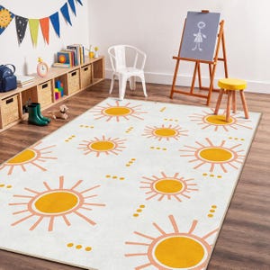 May include: A white rug with a repeating pattern of orange and peach suns. The rug is in a child's playroom, with a wooden easel, a small yellow stool, and a white chair. A shelf with books and toys is visible.