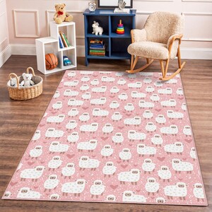 May include: A rectangular pink rug with a repeating pattern of white sheep and small pink hearts. The rug is in a child's room, with a wooden floor and a rocking chair.