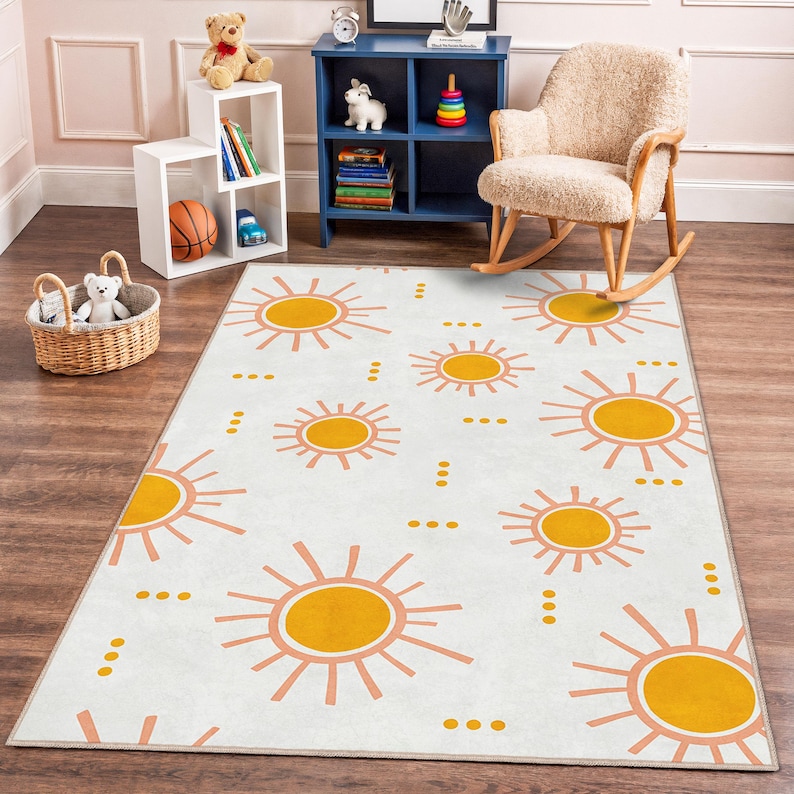 May include: A rectangular area rug with a white background and a repeating pattern of yellow suns with pink rays. The rug is placed on a wooden floor in a child's room.
