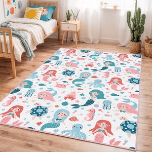 Puede incluir: Alfombra rectangular con un diseño caprichoso de sirenas y criaturas marinas. La alfombra blanca presenta ilustraciones rosas, azules y turquesas de sirenas, pulpos, caballitos de mar y peces. Tiene un borde rosa.