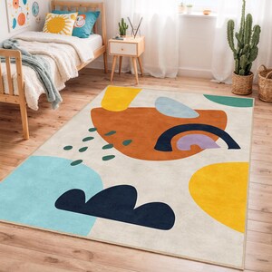 Könnte beinhalten: Ein rechteckiger Teppich mit einem abstrakten Design. Der Teppich zeigt große Formen in Blau-, Gelb-, Orange- und Grüntönen vor einem cremefarbenen Hintergrund. Eine dunkelblaue Bogenform und kleine grüne Tropfenformen ergänzen das Design.
